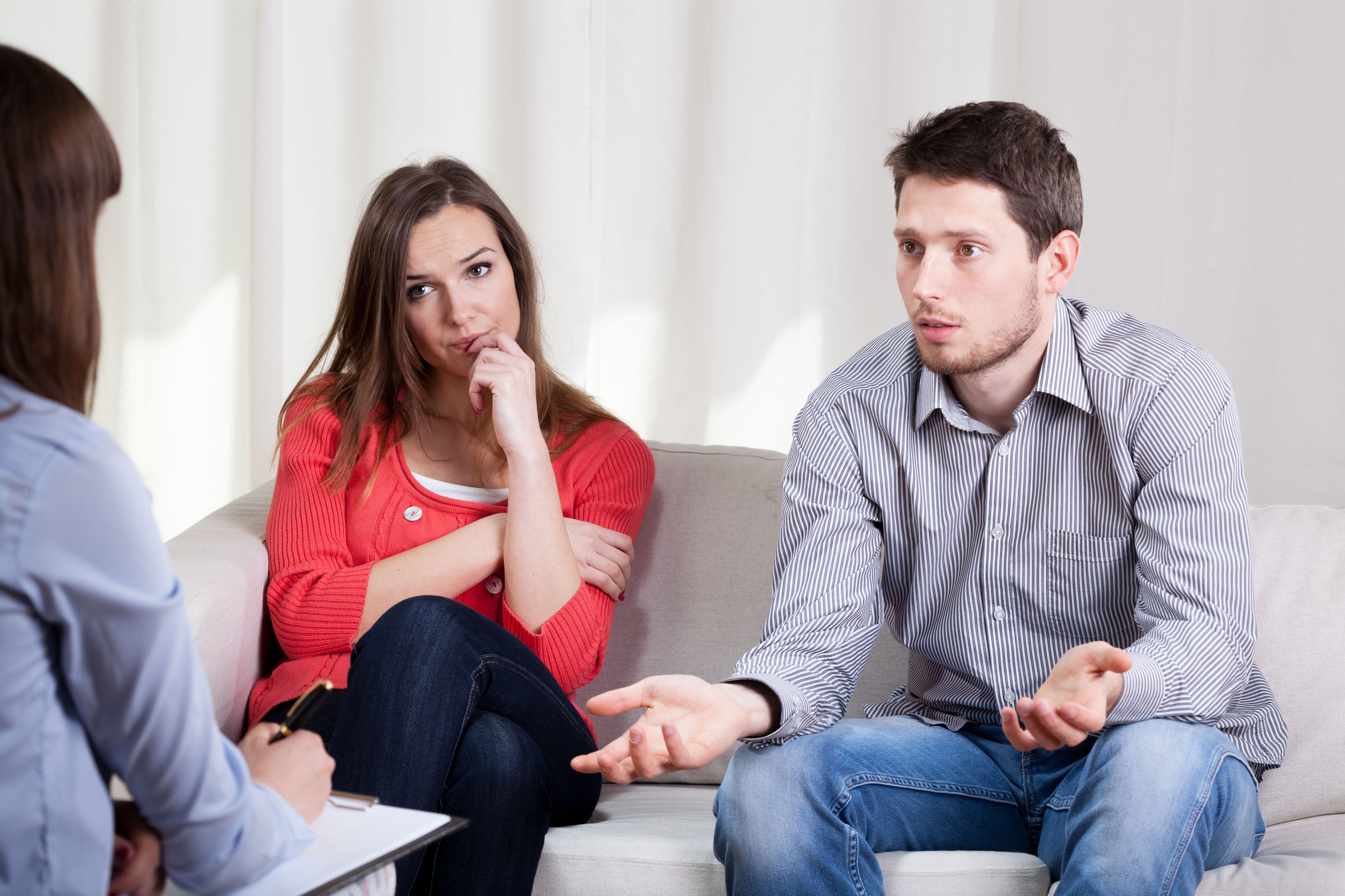  A man and a woman sit on a couch, engaged in conversation, with another woman seated opposite them. 